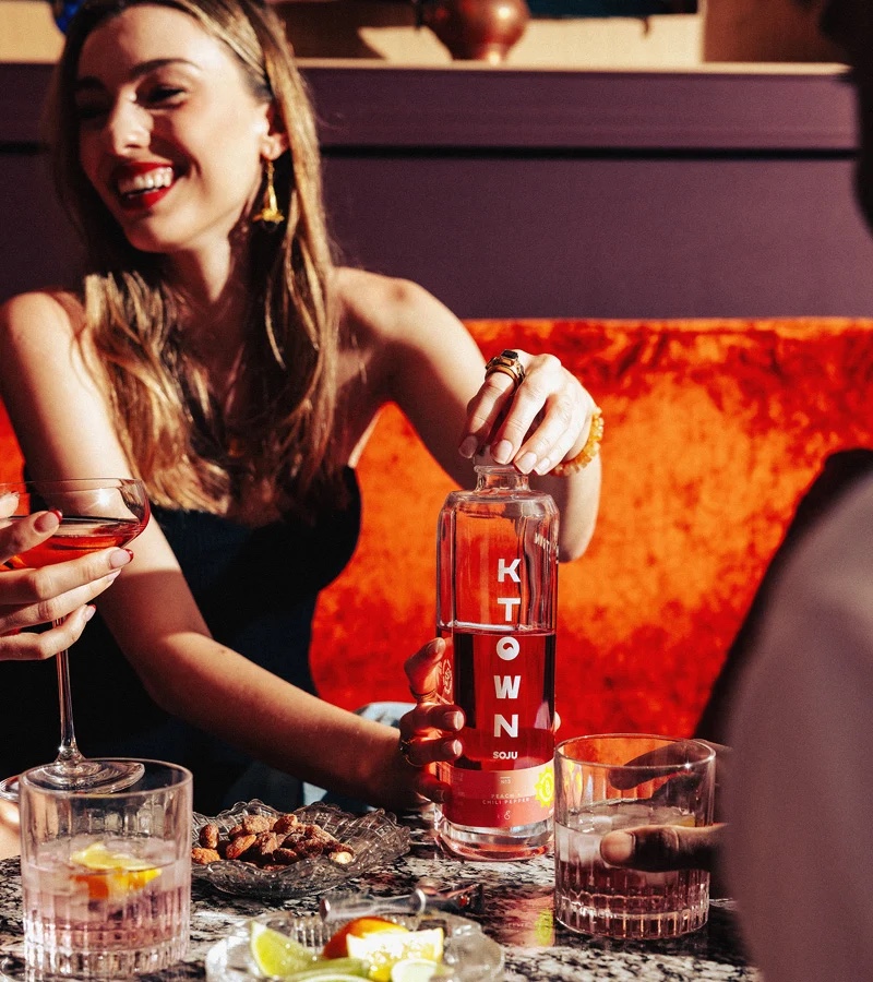 A guest opening a bottle of KTOWN soju around a table with friends